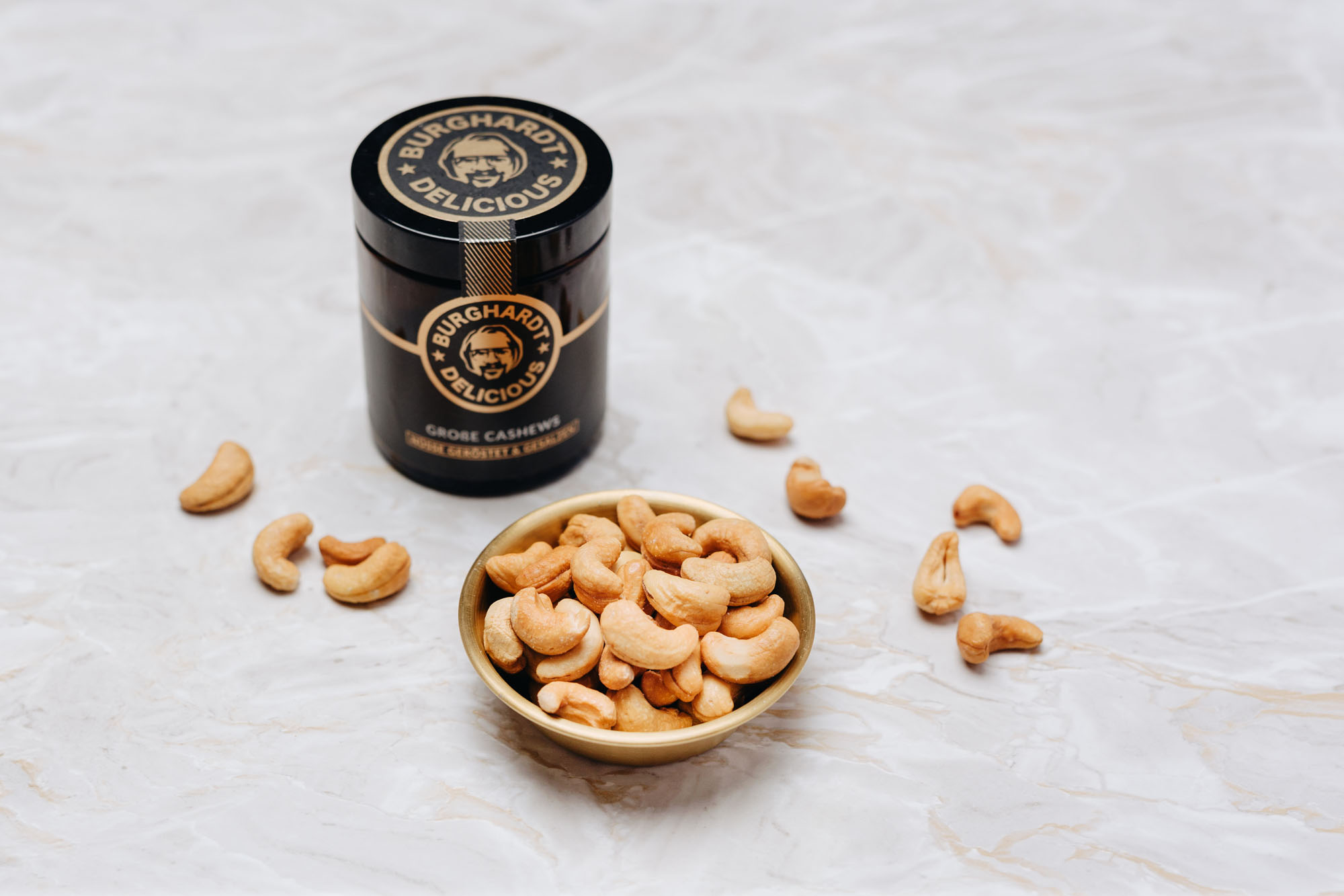 Burghard Delicious Glasdose hinter einer goldenen Schüssel mit Cashews.